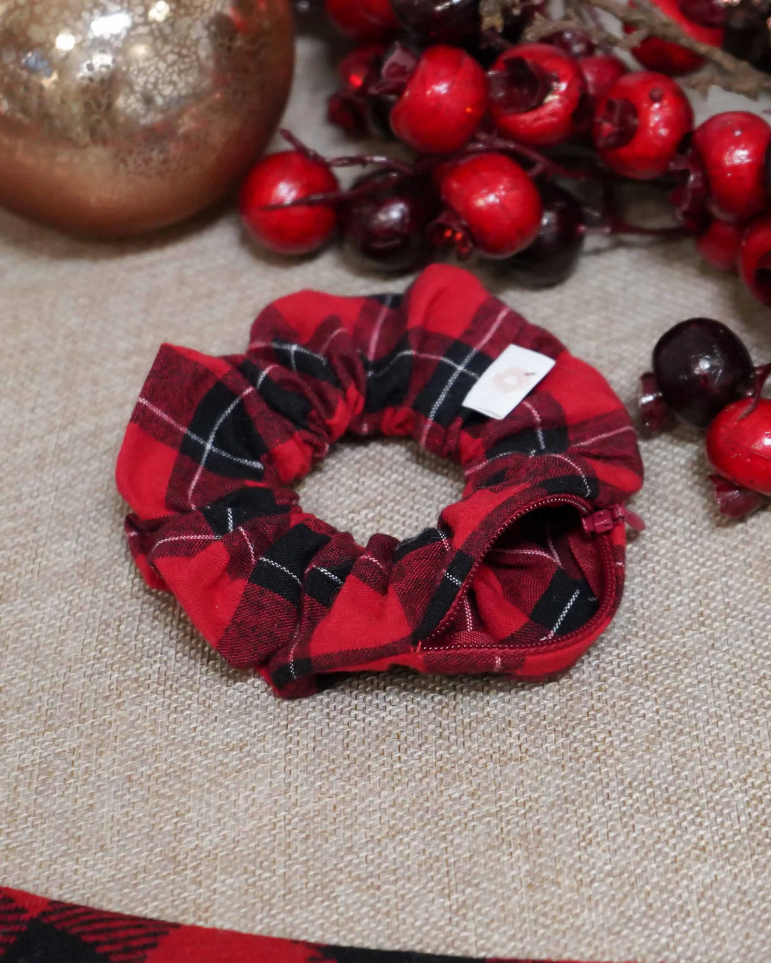 Red flannel holiday scrunchie with a hidden zipper pocket for valuables (cash, keys, AirPods), featuring strong elastic for a secure hold. Inspired by the Christmas season, perfect for workouts, festivals, and holiday events.