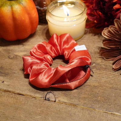 Satin orange fall scrunchie with a hidden zipper pocket for valuables (cash, keys, AirPods), featuring strong elastic for a secure hold, inspired by Halloween, perfect for workouts and festivals.